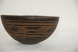 Vintage African wooden bowl, close-up of rim with crack and light brown etched pattern.