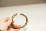 Antique African bronze bracelet held in hand to display its simple, curved form.