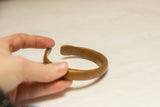 Open cuff of an antique African copper bracelet held by hand, with rich patina.