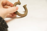 Hand holds vintage African bronze bracelet, highlighting its distinct C-shape and aged patina.