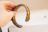 Profile of an antique bronze cuff bracelet showing its substantial C-shape and time-worn patina.