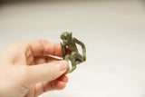 A hand holds the small vintage bronze monkey, showing its scale and oxidized patina.