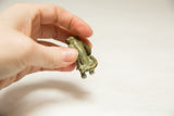 Back of the small oxidized bronze monkey showing aged patina and curled tail, held for scale.