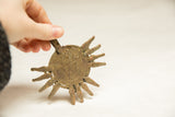 Handheld view of a vintage African bronze medallion with rustic texture and radiating points.