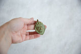 A hand holding a small African bronze mask pendant with a green patina.