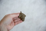 Vintage bronze mask pendant held in a hand to show its small scale and handmade charm.
