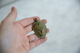 Angled view of the vintage bronze pendant's oxidized green patina and handmade texture.