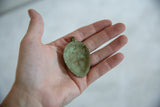 Handmade texture and oxidized green patina on the concave back of a vintage bronze pendant.