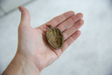 Reverse view of the vintage bronze mask pendant showing its concave, rustic interior.