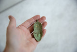 Reverse view of the oxidized bronze mask pendant, showing its concave shape and green patina.
