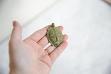 Handmade African bronze mask pendant held to show its scale and textured patina.