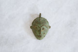 Angled view of the vintage African mask pendant, detailing the textured green bronze patina.