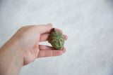 Small African bronze mask pendant with a green patina held in hand for scale.