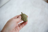 Hand holding the small oxidized bronze mask pendant to show its vintage texture and scale.