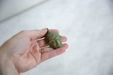 A hand holding the vintage African bronze mask pendant to show its size.