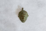 The textured surface and green patina of a vintage African bronze mask pendant.