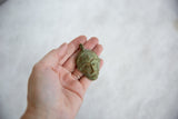 Vintage African bronze mask pendant held in hand to show its patina and scale.