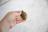 A hand holding the vintage bronze African mask pendant to show its scale and handmade texture.