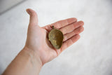 Concave back of a handmade African bronze mask pendant, shown in hand for scale.