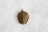 Vintage African bronze mask pendant showing carved facial features and a textured headdress.