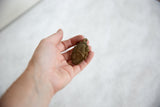 Vintage African bronze mask pendant held in a hand for scale.