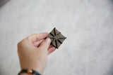 Hand holding the vintage African bronze coin, highlighting its raised, handmade starburst pattern.