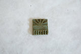 Raised geometric designs and oxidized green patina on a square bronze coin.