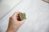Hand holding vintage African square bronze coin, revealing its geometric texture and green patina.