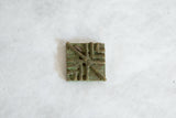 Raised geometric lines and aged green patina on a vintage African bronze coin.