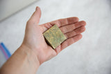 Vintage African square bronze coin resting in a hand to show its scale.