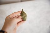 A hand holding the vintage African mask pendant to show its scale and oxidized, textured surface.