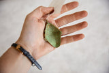 Back of vintage African pendant held in hand, showing its oxidized green patina.