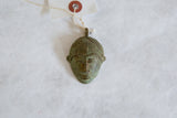 A vintage African mask pendant displaying its handmade texture and oxidized patina.