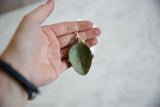 Small handmade African mask pendant with oxidized patina held in hand for scale.