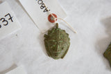The detailed face of a vintage African mask pendant with an aged green patina.