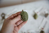 Vintage African mask pendant with a green patina held in a person's hand.