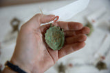 Textured green oxidized finish of a vintage African mask pendant held in hand.