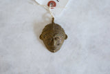 The textured surface and aged patina on a vintage African bronze mask pendant.