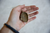 Reverse of the handmade bronze mask pendant, showing its concave form and aged texture.
