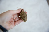 A hand holding the small, textured vintage bronze African mask pendant.