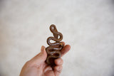 Hand holding the coiled vintage African iron snake, highlighting its dark brown color and textured patina.
