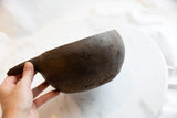 A hand holding the antique wooden pitcher, showing its rounded form and aged patina.