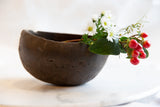 Antique African wooden pitcher styled as a vase with white flowers and red berries.