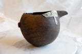 Textured dark wood and a riveted metal patch on an antique African wooden pitcher.
