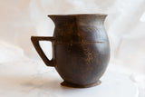 African wooden pitcher's side, featuring its carved handle and prominent surface crack.