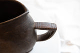 Aged African wooden pitcher side, highlighting a visible crack and hand-carved texture.