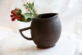Dark, hand-carved texture with visible organic cracks on an antique African wooden pitcher.