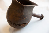Hand-carved lines and textured patina on the body of an antique African wooden pitcher.