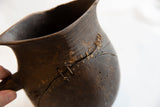 Hand-stitched repair detail on the cracked, textured wood of an antique pitcher.