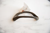The arching shape and rustic, handmade texture of the antique bronze artifact.